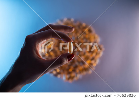 close up of hand holding fish oil capsule or omega 3 vitamins on blue background 76629820