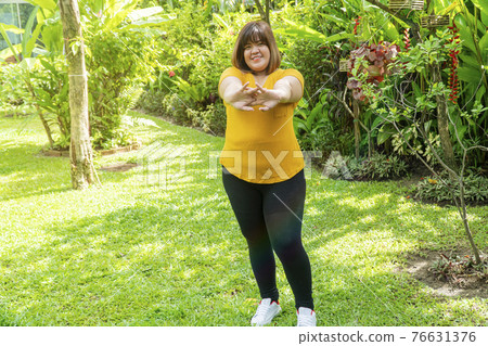 Healthy weight loss concept. Happy overweight young woman stretching before workout in the garden. 76631376