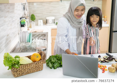 mother looking at recipe from laptop and cooking with her daughter 76637274