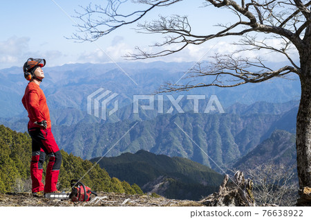 A male forestry worker arriving at the top of a mountain that has been maintained and looking up at the sun 76638922