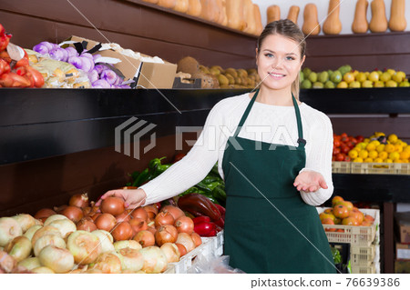 Glad female seller standing near vegetables 76639386