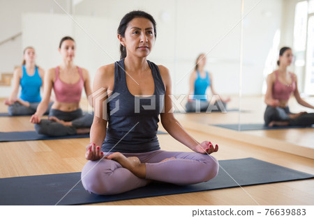 Hispanic woman meditating in yoga position Padmasana during group training 76639883