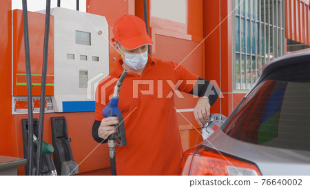 A Caucasian man, people, worker filling up fuel by using petrol pump at gasoline petrol station, wearing a face mask. refuel petroleum oil and energy vehicle business service. Coronavirus pandemic. A Caucasian man, people, worker filling up fuel by using petrol pump at gasoline petrol station, wearing a face mask. refuel petroleum oil and energy vehicle business service. Coronavirus pandemic. 76640002