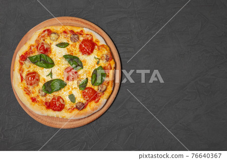 Pizza on wooden plate on black stone background. Cheese pizza with tomato, mozzarella and basil. Close-up photo. Copy space. Pizza on wooden plate on black stone background. Cheese pizza with tomato, mozzarella and basil. Close-up photo. Copy space. 76640367