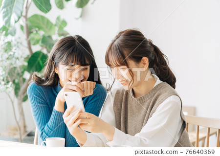 Two smiling women looking at a smartphone at a cafe Two smiling women looking at a smartphone at a cafe 76640369