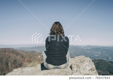 girl from the back sitting on a top stone looking at the mountains 76647665