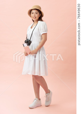 Full length image of Smiling asian woman in hat with retro camera holding passport with tickets and looking camera over pink background 76649630