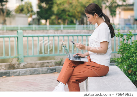 Shopper girl buying online with a laptop and credit card sitting in a park in summer 76649632