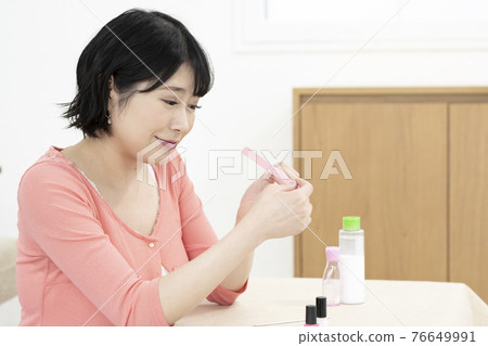 A young woman caring for her nails with a nail file in the room A young woman caring for her nails with a nail file in the room 76649991