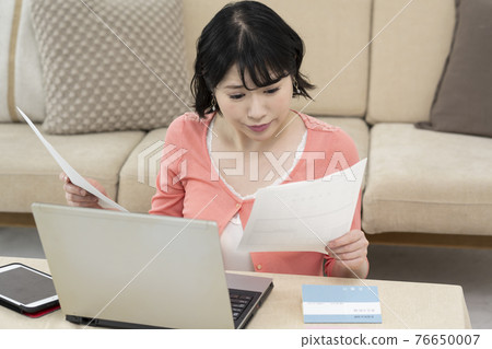 一位女士一邊在客廳裡看材料,一邊在筆記本電腦上打字 一位女士一邊在客廳裡看材料,一邊在筆記本電腦上打字 76650007
