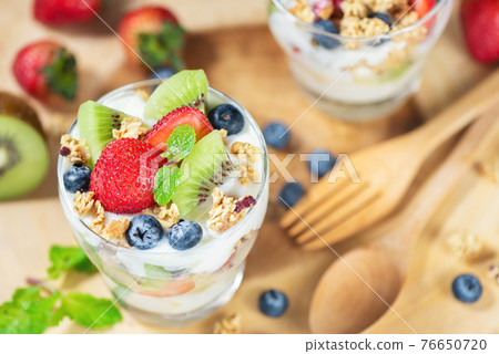 Fresh fruit salad with yogurt and berry in glass on wooden plate 76650720