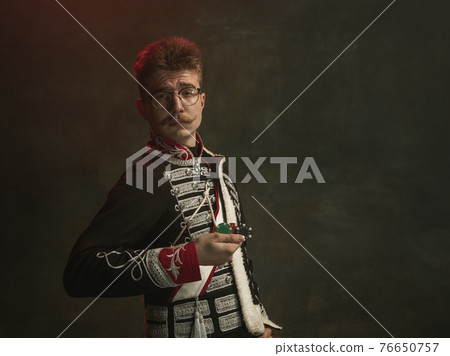 Young man in suit as royal person isolated on dark green background. Retro style, comparison of eras concept. Beautiful male model like historical character, monarch, old-fashioned. Young man in suit as royal person isolated on dark green background. Retro style, comparison of eras concept. Beautiful male model like historical character, monarch, old-fashioned. 76650757