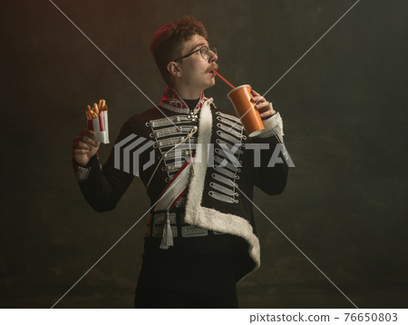 Young man in suit as royal person isolated on dark green background. Retro style, comparison of eras concept. Beautiful male model like historical character, monarch, old-fashioned. 76650803