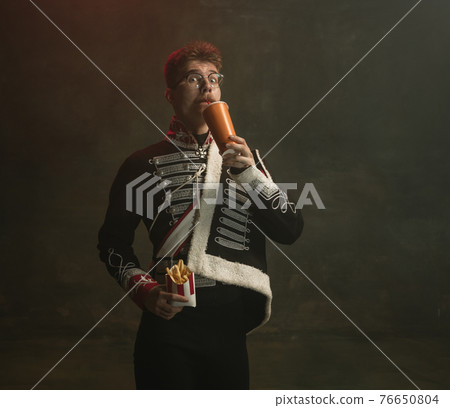 Young man in suit as royal person isolated on dark green background. Retro style, comparison of eras concept. Beautiful male model like historical character, monarch, old-fashioned. 76650804