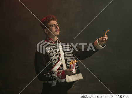 Young man in suit as royal person isolated on dark green background. Retro style, comparison of eras concept. Beautiful male model like historical character, monarch, old-fashioned. 76650824