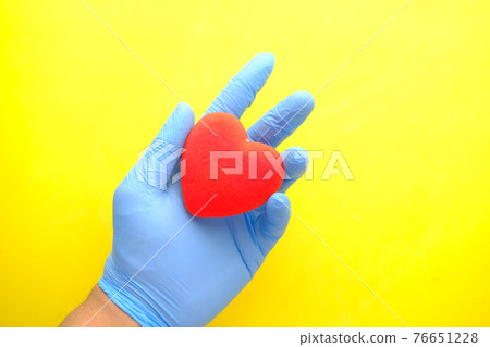 man hand in protective gloves holding red heart on yellow background  76651228