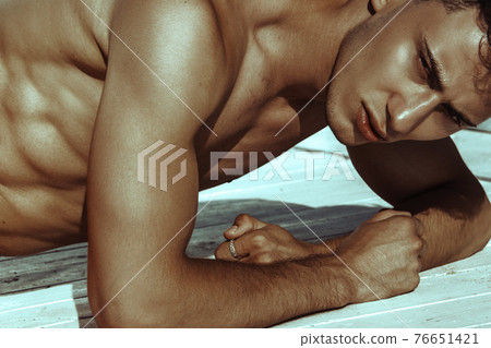 Strong face muscle male model in the open  summer shower on the vacation pool background with blue water on the nature beach on the sunset 76651421