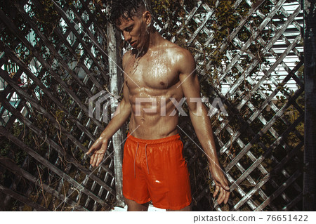 Strong face muscle male model in the open summer shower on the vacation pool background with blue water on the nature beach on the sunset Strong face muscle male model in the open summer shower on the vacation pool background with blue water on the nature beach on the sunset 76651422