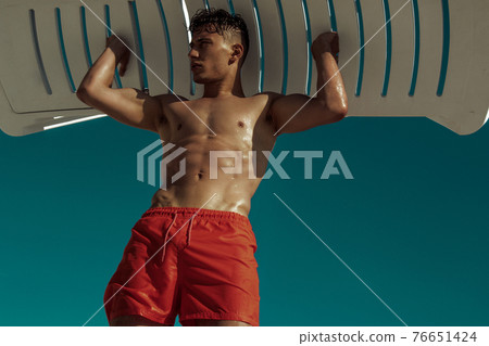 Strong face muscle male model in the open summer shower on the vacation pool background with blue water on the nature beach on the sunset Strong face muscle male model in the open summer shower on the vacation pool background with blue water on the nature beach on the sunset 76651424