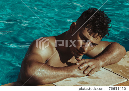 Strong face muscle male model in the open summer shower on the vacation pool background with blue water on the nature beach on the sunset Strong face muscle male model in the open summer shower on the vacation pool background with blue water on the nature beach on the sunset 76651430