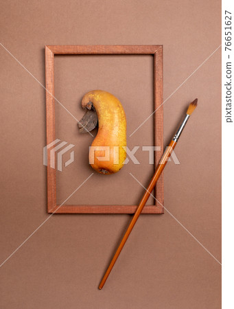 Wooden frame with ugly ripe pear inside it and brush on brown background. Healthy natural organic fruits. Waste zero food concept. Food as art. Top view. Vertical orientation. Wooden frame with ugly ripe pear inside it and brush on brown background. Healthy natural organic fruits. Waste zero food concept. Food as art. Top view. Vertical orientation. 76651627