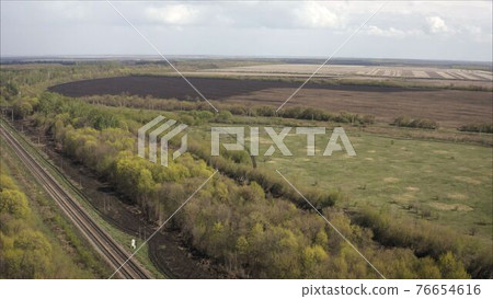 A railway track passing through the forest and field. Shooting from a height. Russian railway, taken from a height. A railway track passing through the forest and field. Shooting from a height. Russian railway, taken from a height. 76654616