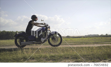 Motorcyclist rides on the field. The concept of adventure. Motorcyclist rides on a country road in the summer. Motorcyclist rides on the field. The concept of adventure. Motorcyclist rides on a country road in the summer. 76654692