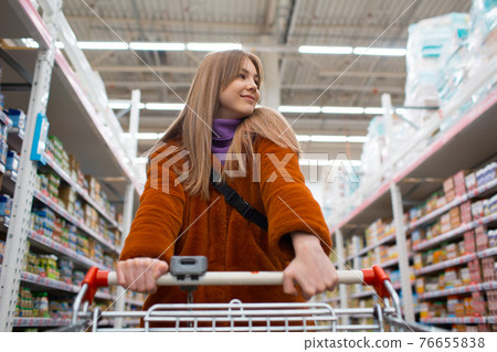 Woman with shopping cart at retail store shelves Woman with shopping cart at retail store shelves 76655838