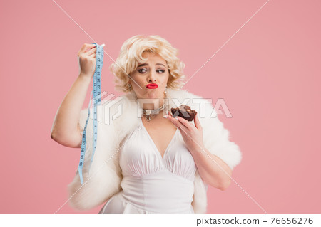 Portrait of young woman in white dress on coral pink background. Female model as a legendary actress. Pin up. Concept of comparison of eras, modern, fashion, beauty. 76656276