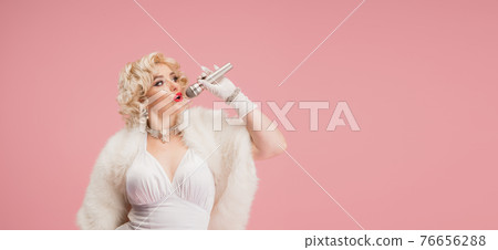 Portrait of young woman in white dress on coral pink background. Female model as a legendary actress. Pin up. Concept of comparison of eras, modern, fashion, beauty. Portrait of young woman in white dress on coral pink background. Female model as a legendary actress. Pin up. Concept of comparison of eras, modern, fashion, beauty. 76656288