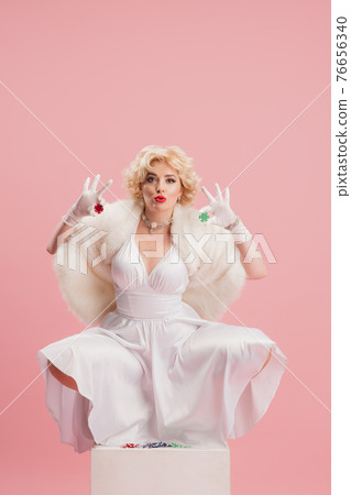 Portrait of young woman in white dress on coral pink background. Female model as a legendary actress. Pin up. Concept of comparison of eras, modern, fashion, beauty. Portrait of young woman in white dress on coral pink background. Female model as a legendary actress. Pin up. Concept of comparison of eras, modern, fashion, beauty. 76656340