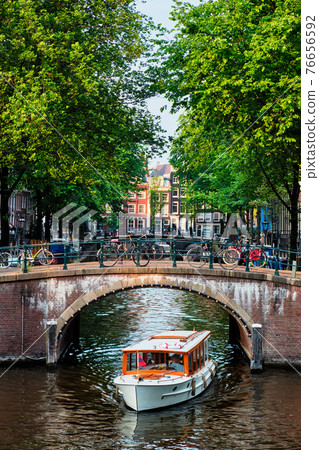 Amsterdam view - canal with boad, bridge and old houses 76656592