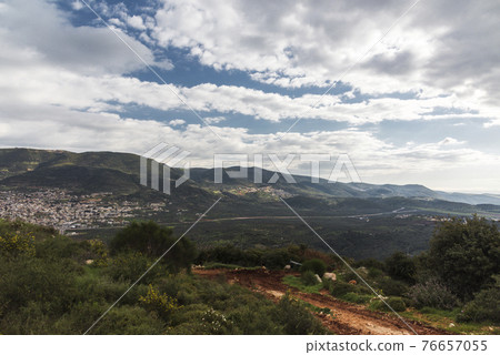 A view of a mountain range and a green valley in the morning at sunrise, against a dramatic back of blue skies and clouds. High quality photo. Travel concept hiking. North District Israel 76657055
