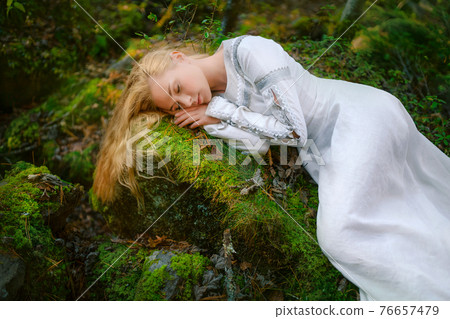 Beautiful young woman in a white dress in the middle of a forest Beautiful young woman in a white dress in the middle of a forest 76657479