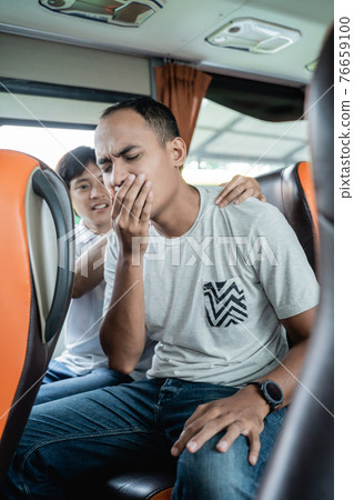 a travel sick young man and his friend massage his back while sitting on a bus bench a travel sick young man and his friend massage his back while sitting on a bus bench 76659100