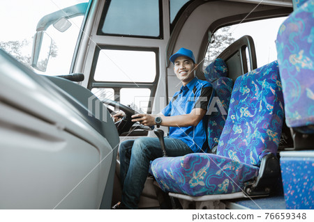 A male driver in a uniform and hat smiles at the camera 76659348