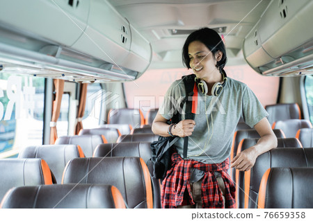 close up of a young man wearing a backpack and headphones standing looking at his seat 76659358