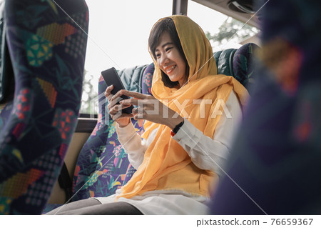 muslim woman using her mobile phone while riding a bus 76659367