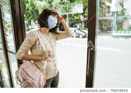 Asian woman wearing a mask stands waiting for the bus Asian woman wearing a mask stands waiting for the bus 76659640
