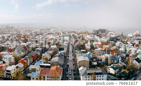 The snow covered rooftops of Reykjavik, historic capital city of Iceland. Traditional houses, aerial view, with the coastline, sea and mountains beyond. The snow covered rooftops of Reykjavik, historic capital city of Iceland. Traditional houses, aerial view, with the coastline, sea and mountains beyond. 76661817