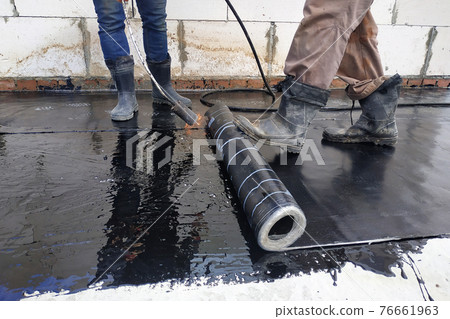 The workers cover the concrete screed with bituminous liquid solution and stele the waterproofing. The workers cover the concrete screed with bituminous liquid solution and stele the waterproofing. 76661963