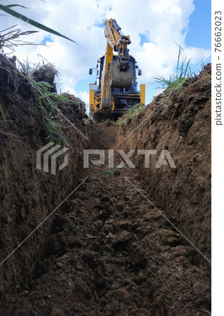 A yellow excavator digging a trench on the construction site, a close-up, against the sky. 76662023