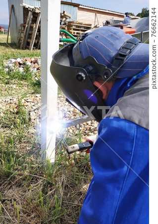 In the village on the construction site, a welder welds a fence. In the village on the construction site, a welder welds a fence. 76662144