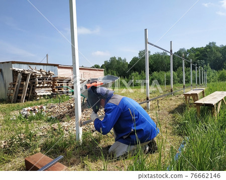 A fence installer welds a metal profile to a new fence post. A fence installer welds a metal profile to a new fence post. 76662146