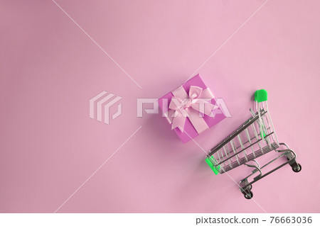 Shopping cart and gift wrap with bow on light pink background 76663036