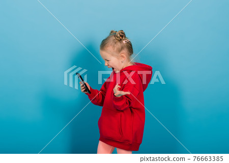 Smiling little girl on the phone over blue background Smiling little girl on the phone over blue background 76663385