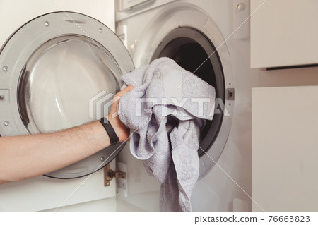 Man loading color clothes and towels into built-in washing machine 76663823