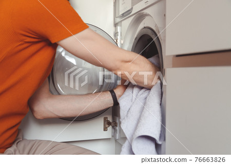 Man loading color clothes and towels into built-in washing machine 76663826