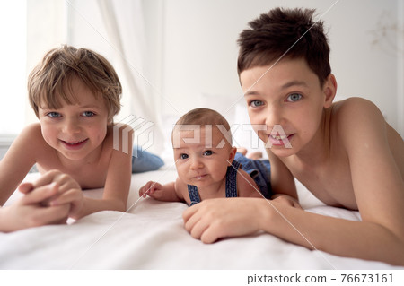 Three funny brothers boys are lying on the bed and having fun 76673161