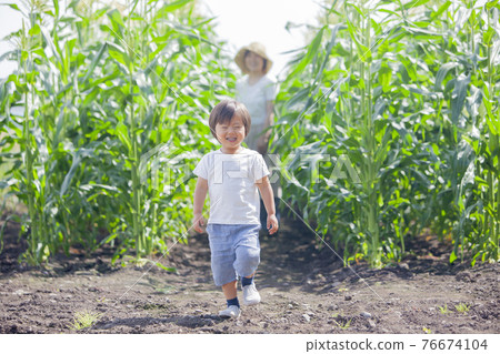 A farmer's mother working in the field and a child playing in the field 76674104